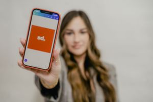 Person holding smartphone displaying orange mobile app screen against light background.