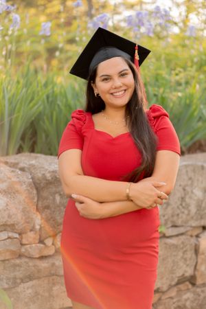 Graduate in red dress poses outdoors for graduation photos with natural background.