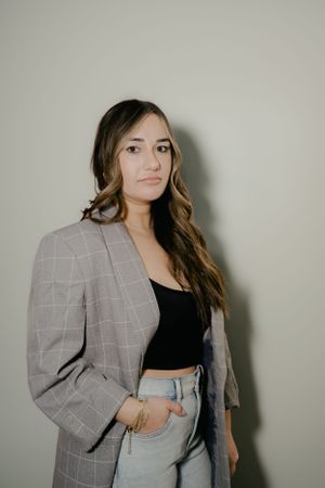 Fashion model wearing grey plaid blazer and light denim in studio setting.