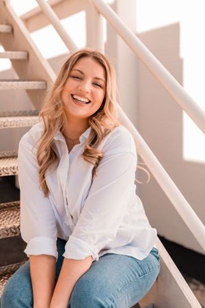 A relaxed portrait on stairs featuring a white shirt, jeans, and warm natural lighting.
