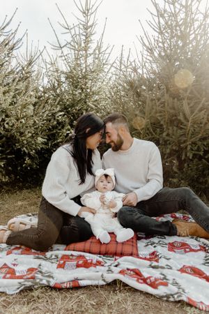 Intimate family moment on red and white blanket surrounded by evergreen trees.