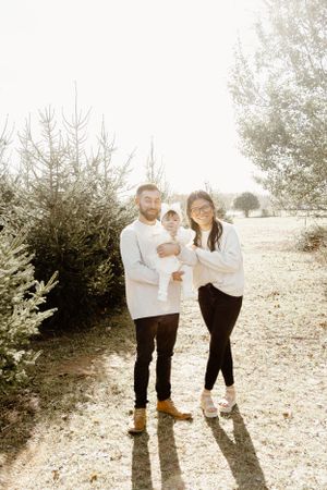 Family portrait outdoors with evergreen trees and long shadows on sunny day.