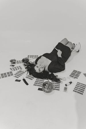 Black and white artistic photo of person lying on floor surrounded by scattered papers and a clock in minimalist setting.