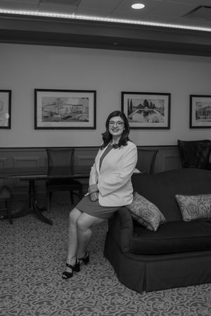 Professional woman in white blazer posing confidently in an elegant office lounge with framed artwork.