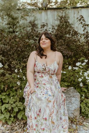 A floral summer dress flows gracefully in a garden setting with white flowers and greenery in the background.