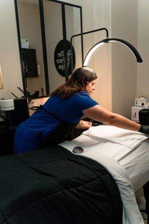 Massage therapist preparing white sheets on a treatment table in a spa setting.