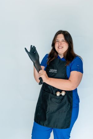 Healthcare worker in blue uniform and black apron putting on disposable gloves.