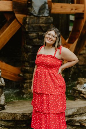 A person wearing a red polka dot tiered summer dress poses against a rustic outdoor background.