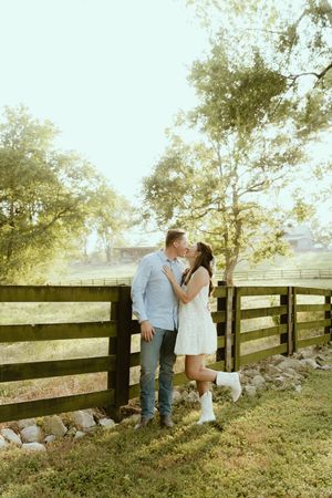 A romantic couple shares tender moments by a wooden fence at sunset in a dreamy countryside setting.