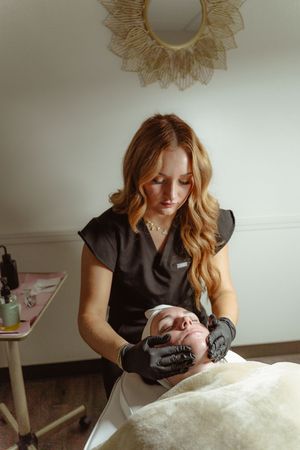 A massage therapist in black attire performs a relaxing facial treatment on a client in a serene spa setting.