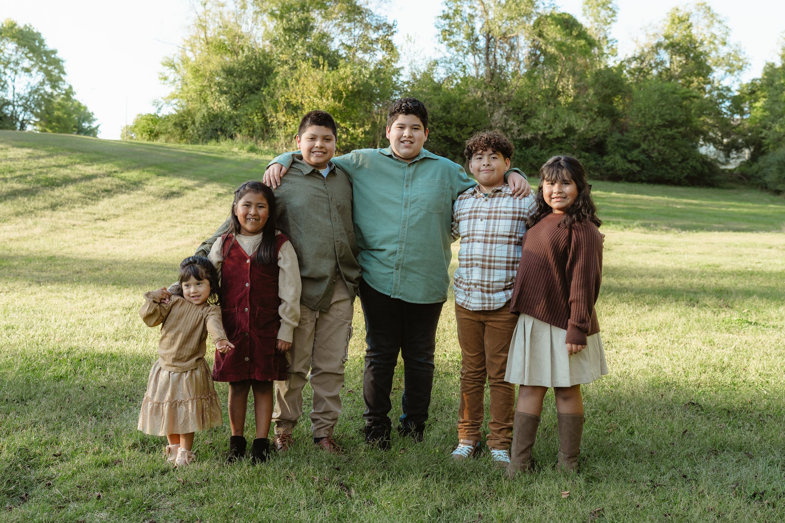 A family of five poses together outdoors on a grassy hillside on a sunny day.