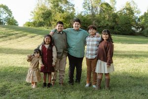 A family of five poses together outdoors on a grassy hillside on a sunny day.