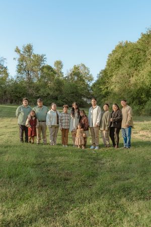 A group of people standing together on a grassy field with trees in the background on a sunny day.