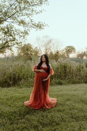A person in a flowing rust-colored dress twirls gracefully in a misty meadow at sunset.