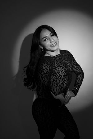 Black and white portrait of a smiling woman in leopard print top, posing confidently against a spotlight background.