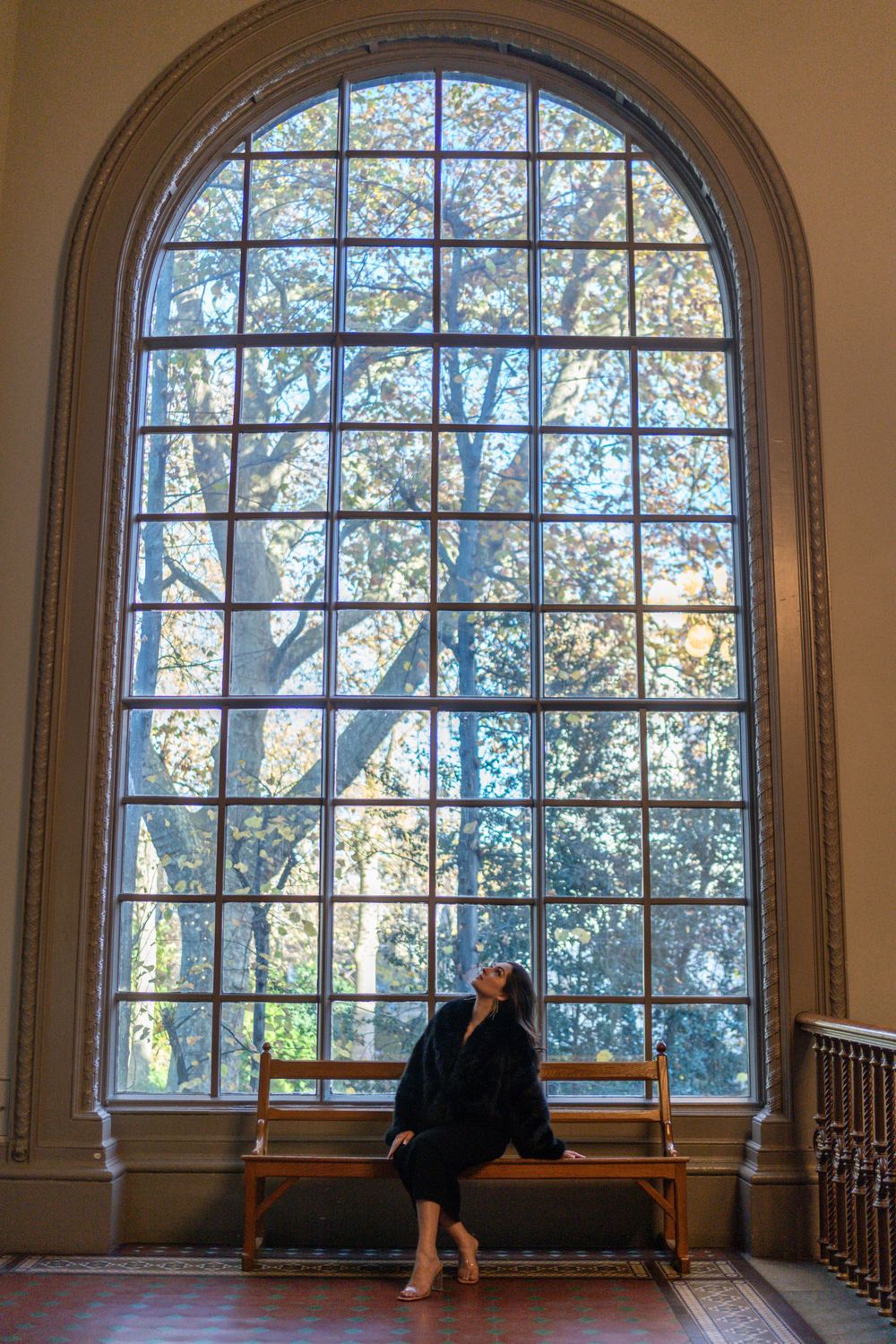 Figure seated beneath tall arched window with sunlight filtering through gridded glass.