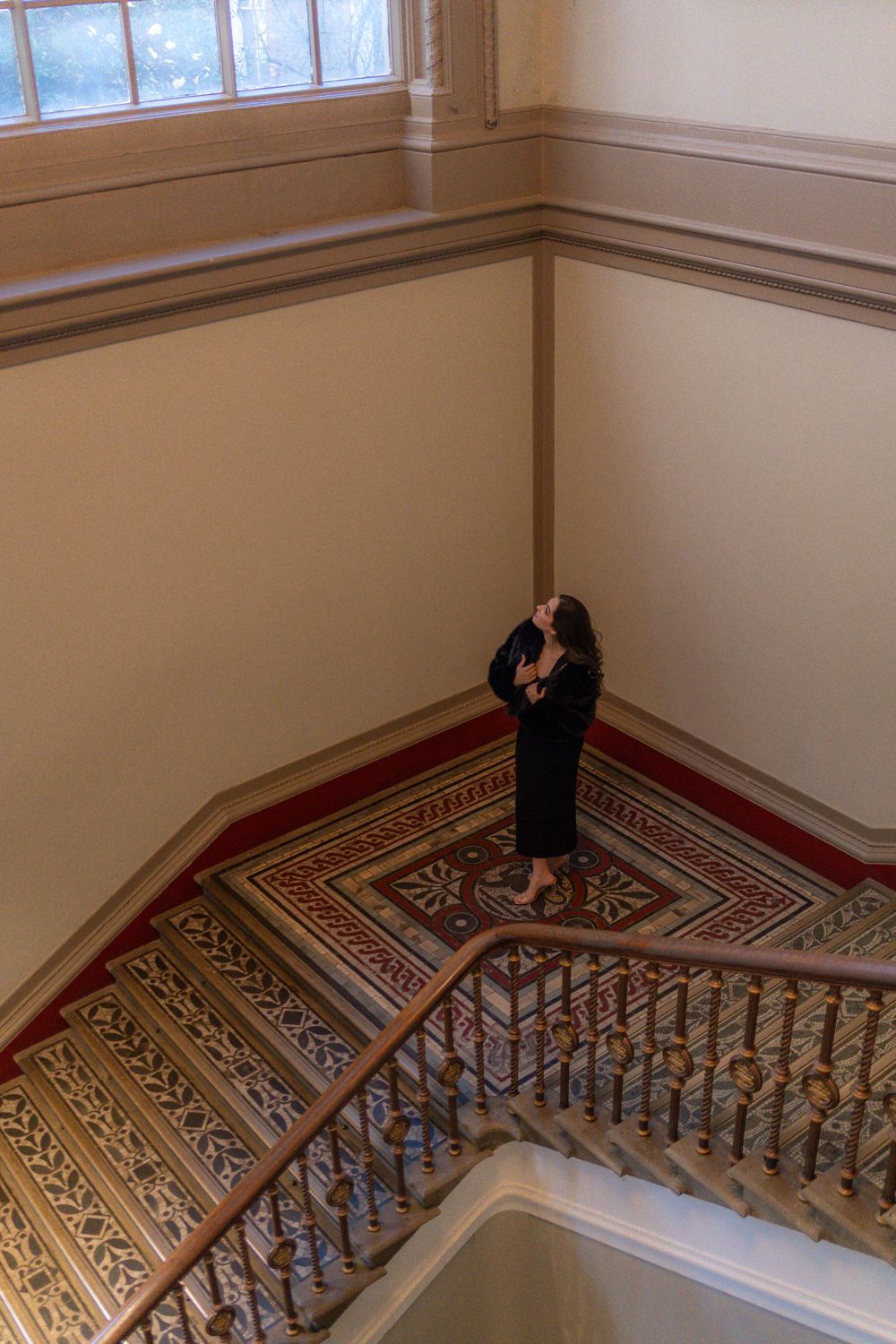 Figure stands on patterned staircase landing viewed from above in historic building.