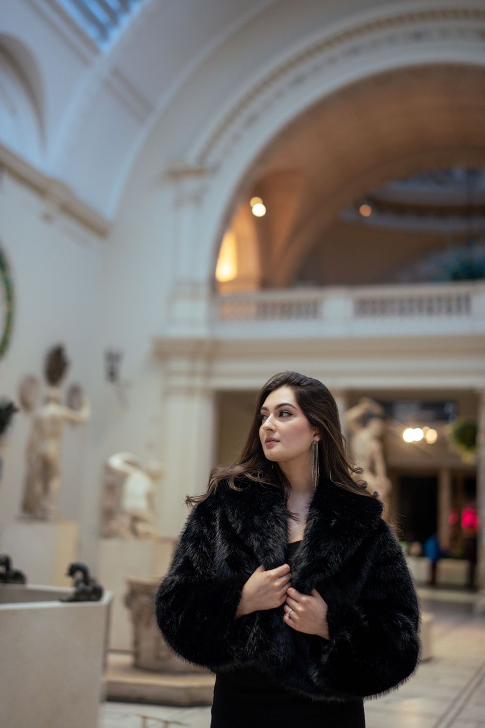 Dramatic fashion portrait in museum interior with arched ceilings and classical sculptures.