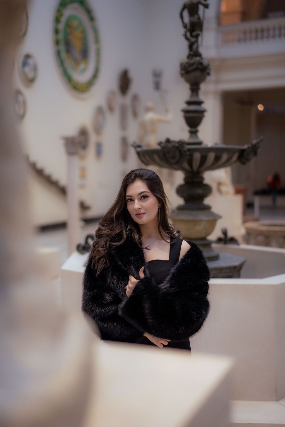 Artistic portrait near vintage fountain with decorative plates and classical architecture.