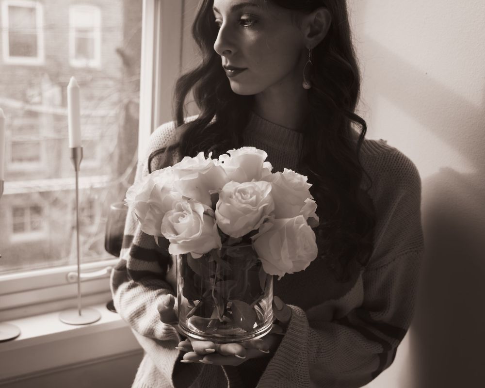 Artistic black and white photo featuring white roses in a glass vase by a window.