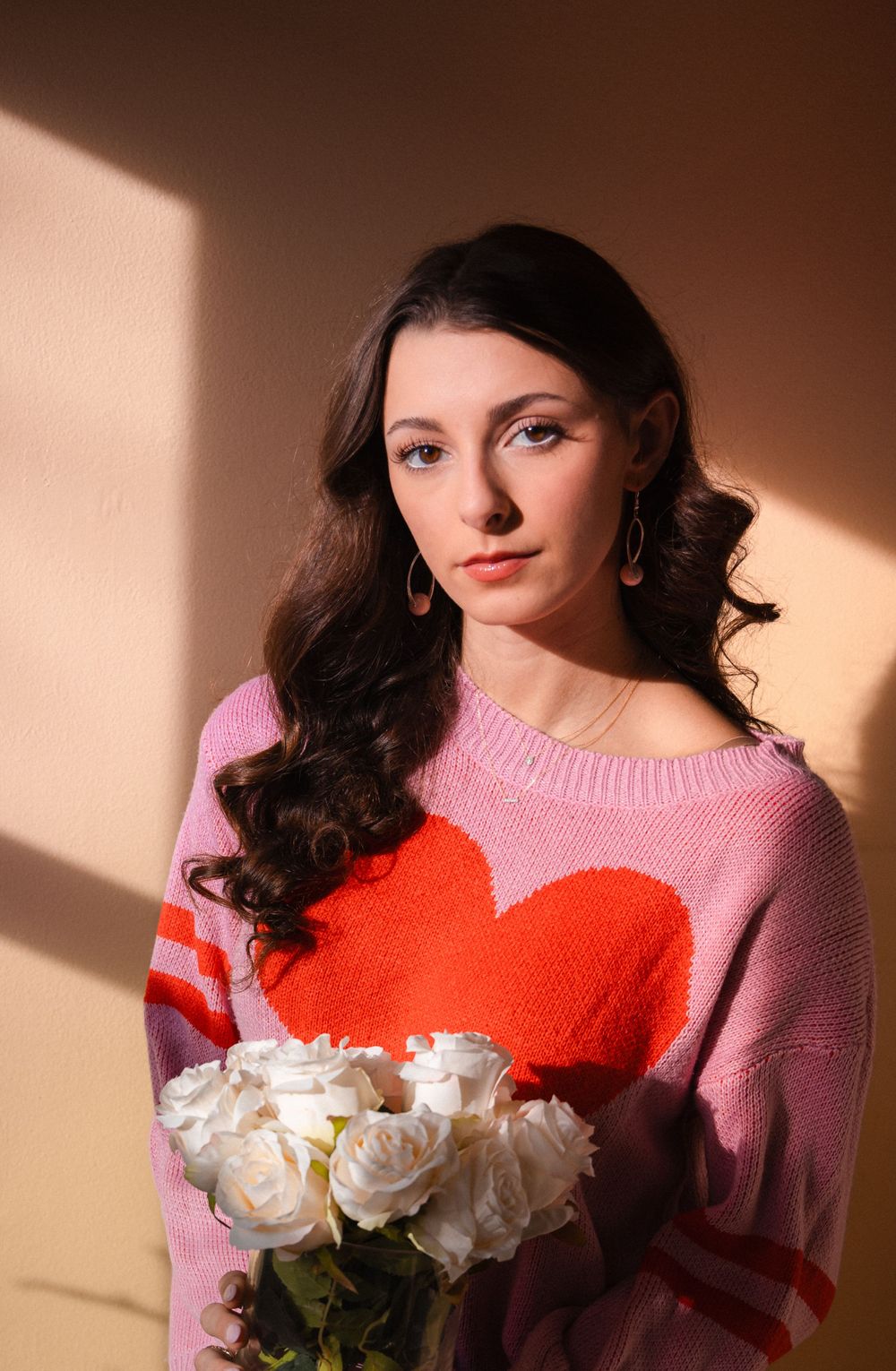 Fashion portrait with pink heart sweater and white roses in warm lighting.