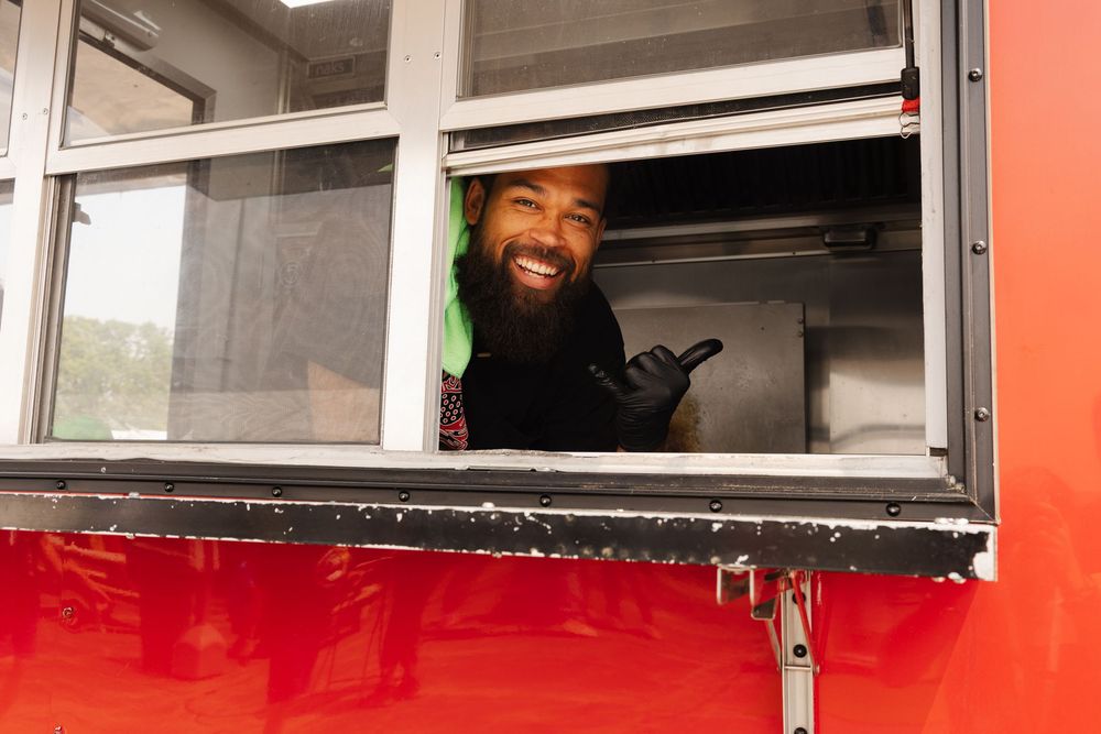 Red food truck window with staff serving customers outdoors.