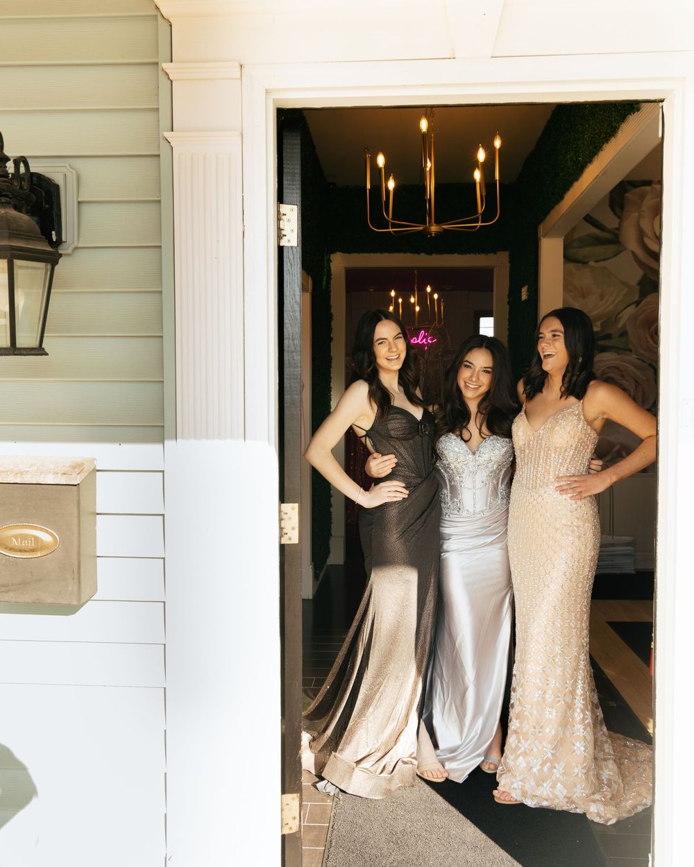 Three formal dresses in black, silver, and champagne colors photographed in an elegant doorway.