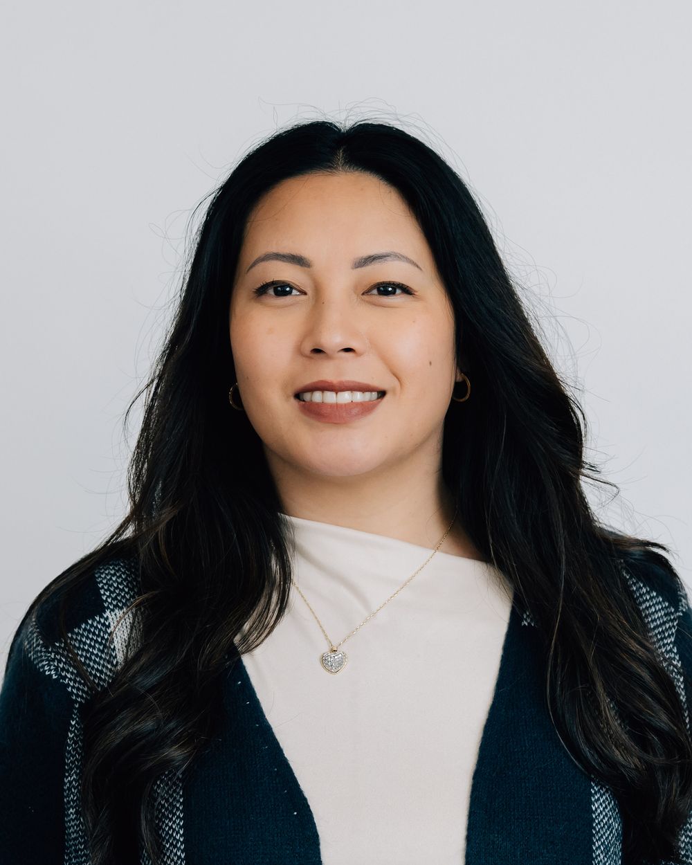 Professional headshot of smiling woman with long black hair wearing teal cardigan.