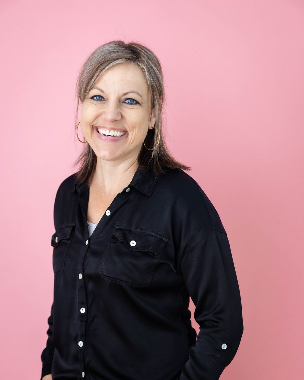 Smiling woman in black shirt posing against bright pink background.