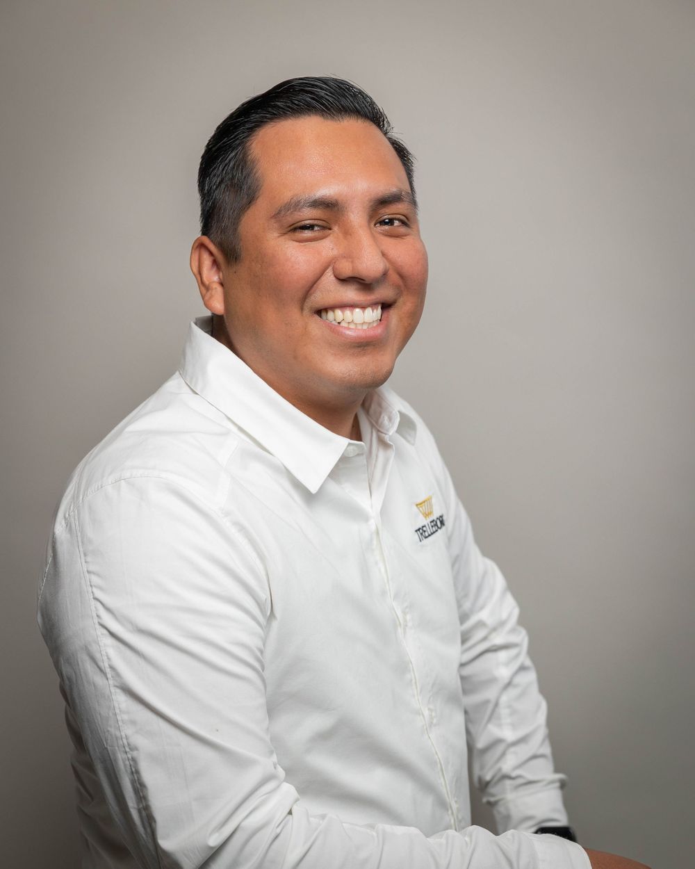 Friendly smiling Hispanic man in white Trelleborg shirt posing for professional corporate headshot.