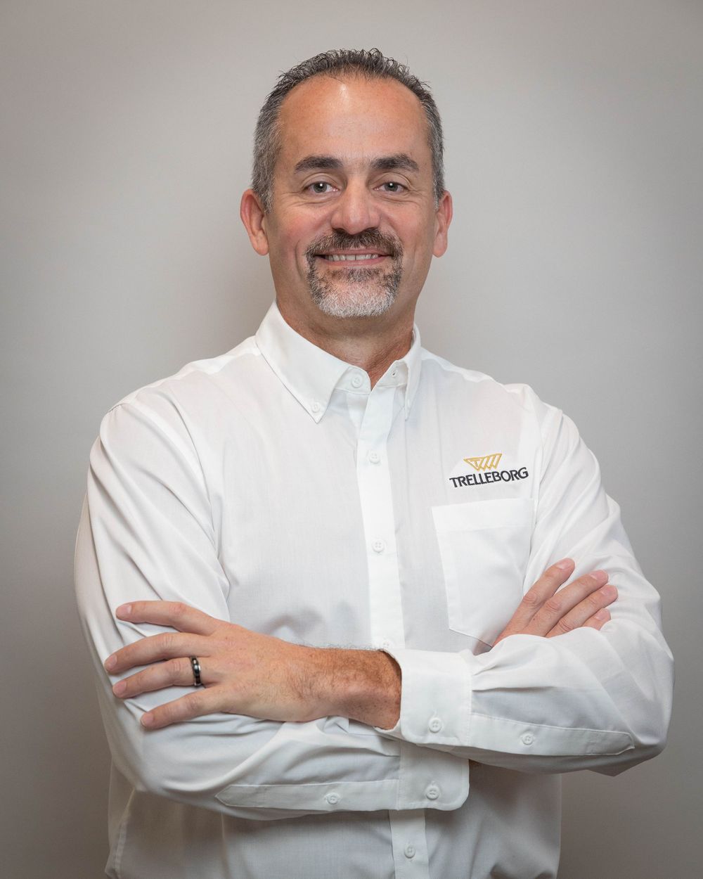 Professional portrait of a smiling man in white Trelleborg shirt with arms crossed confidently.