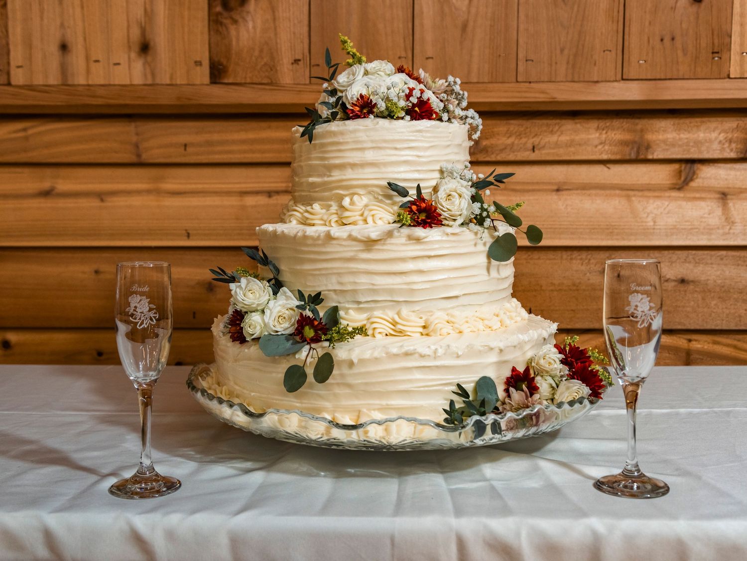 Elegant three-tier wedding cake decorated with fresh flowers and eucalyptus on white tablecloth.