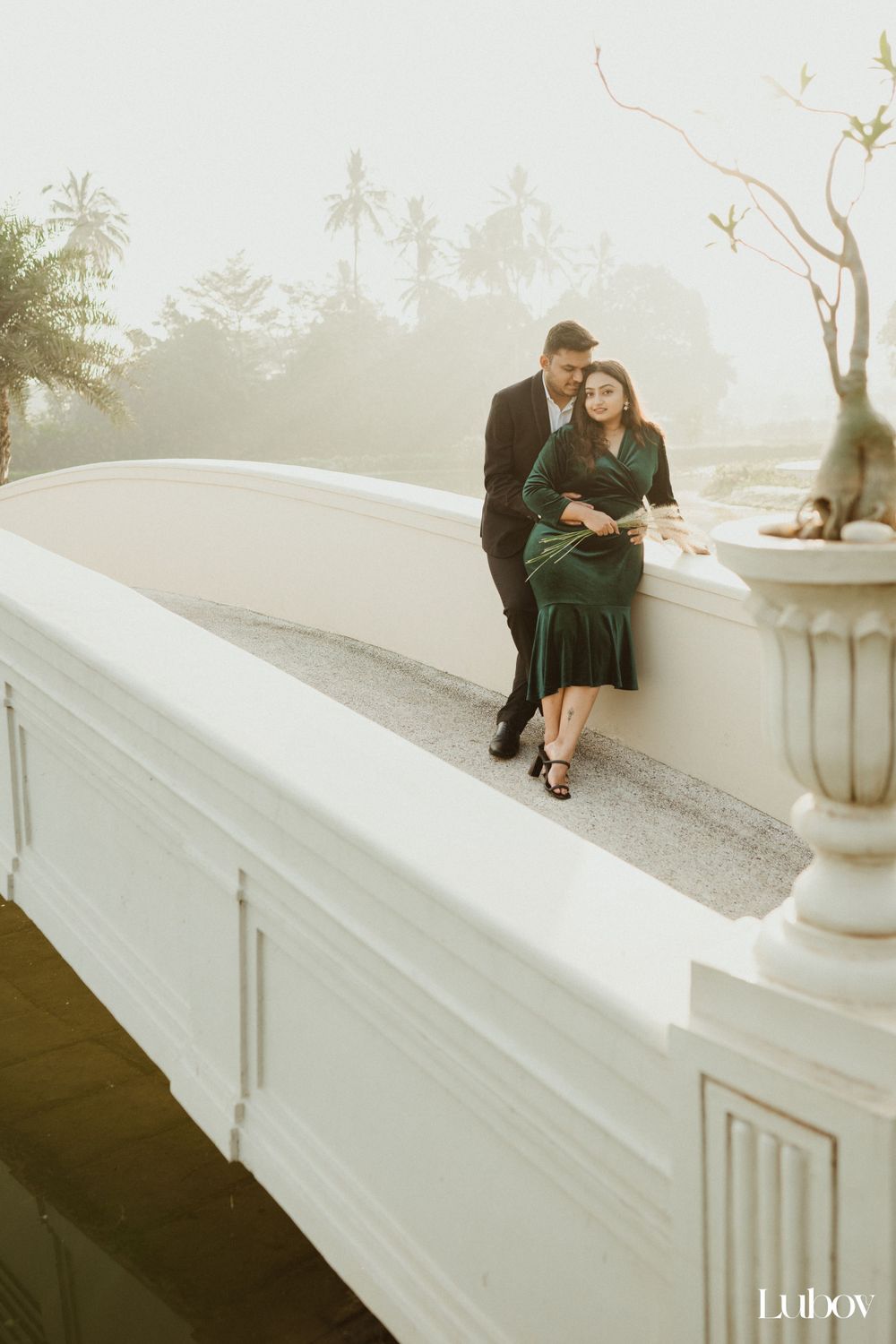 Romantic couple pose on white curved wall during sunset with tropical backdrop.