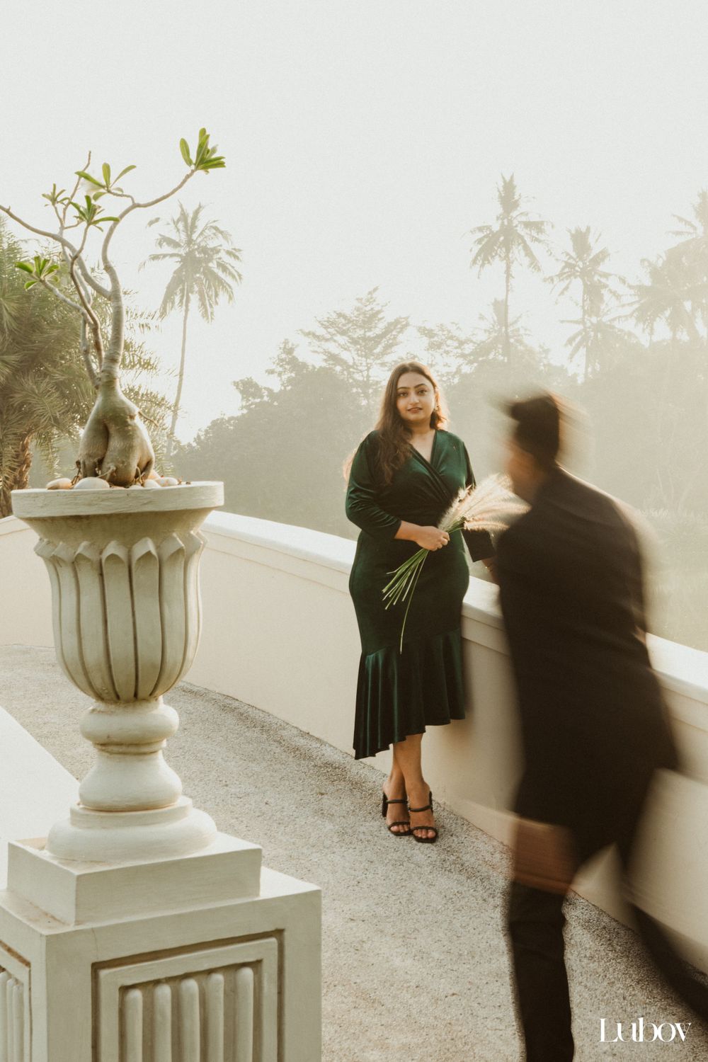 Stylish photoshoot near classical stone urn with palm trees in misty background.