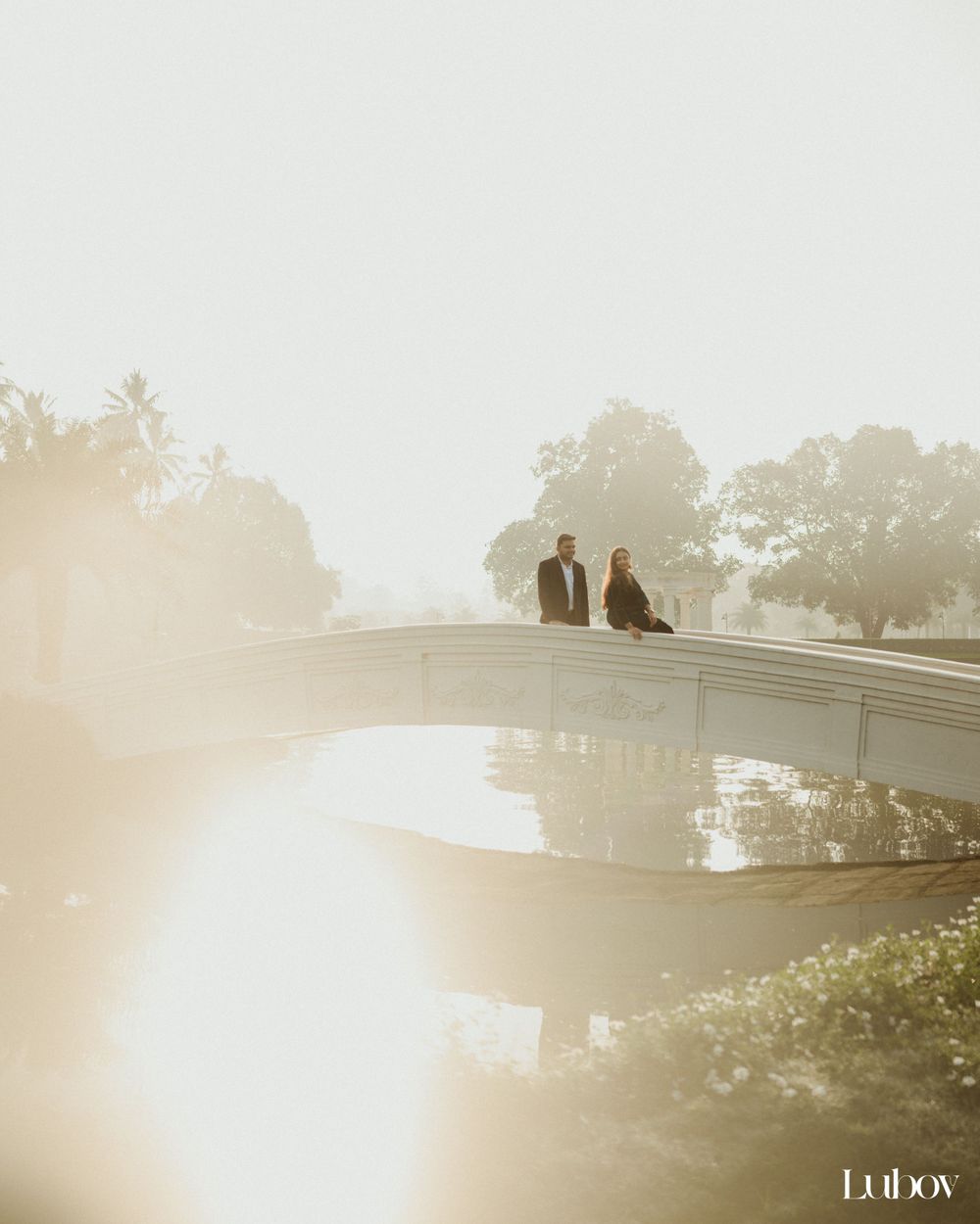 Silhouetted figures on curved bridge during misty sunset with sunburst effect.