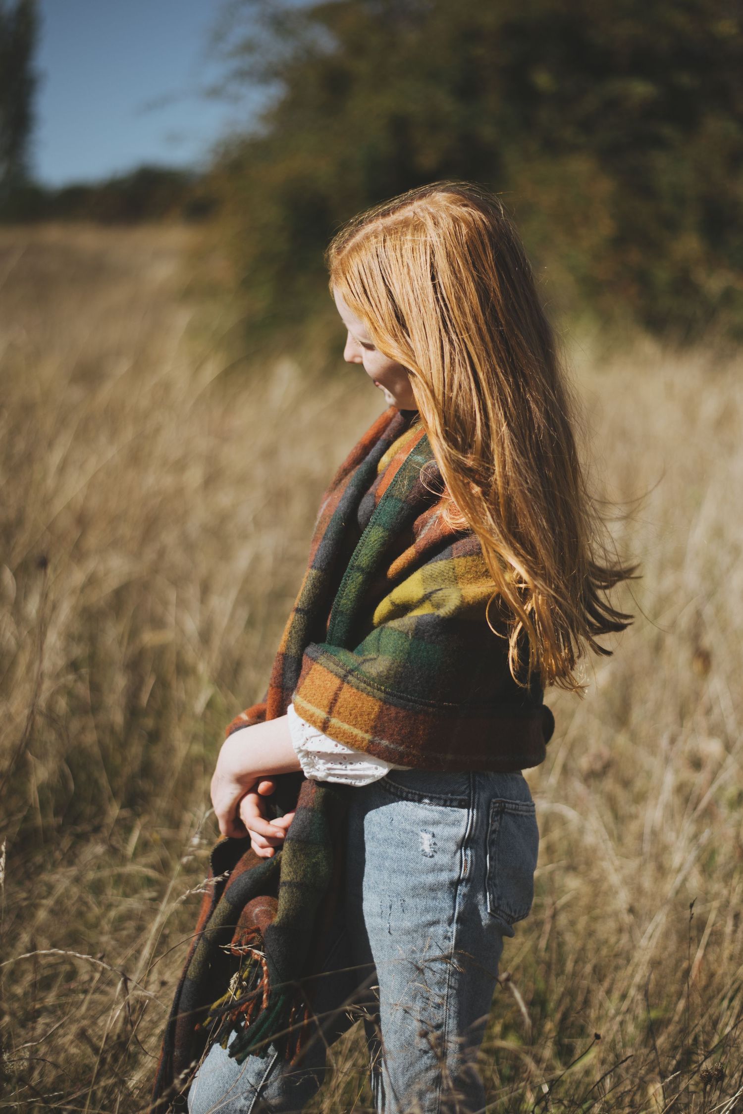 Figure standing in tall golden grass wearing plaid jacket and jeans.