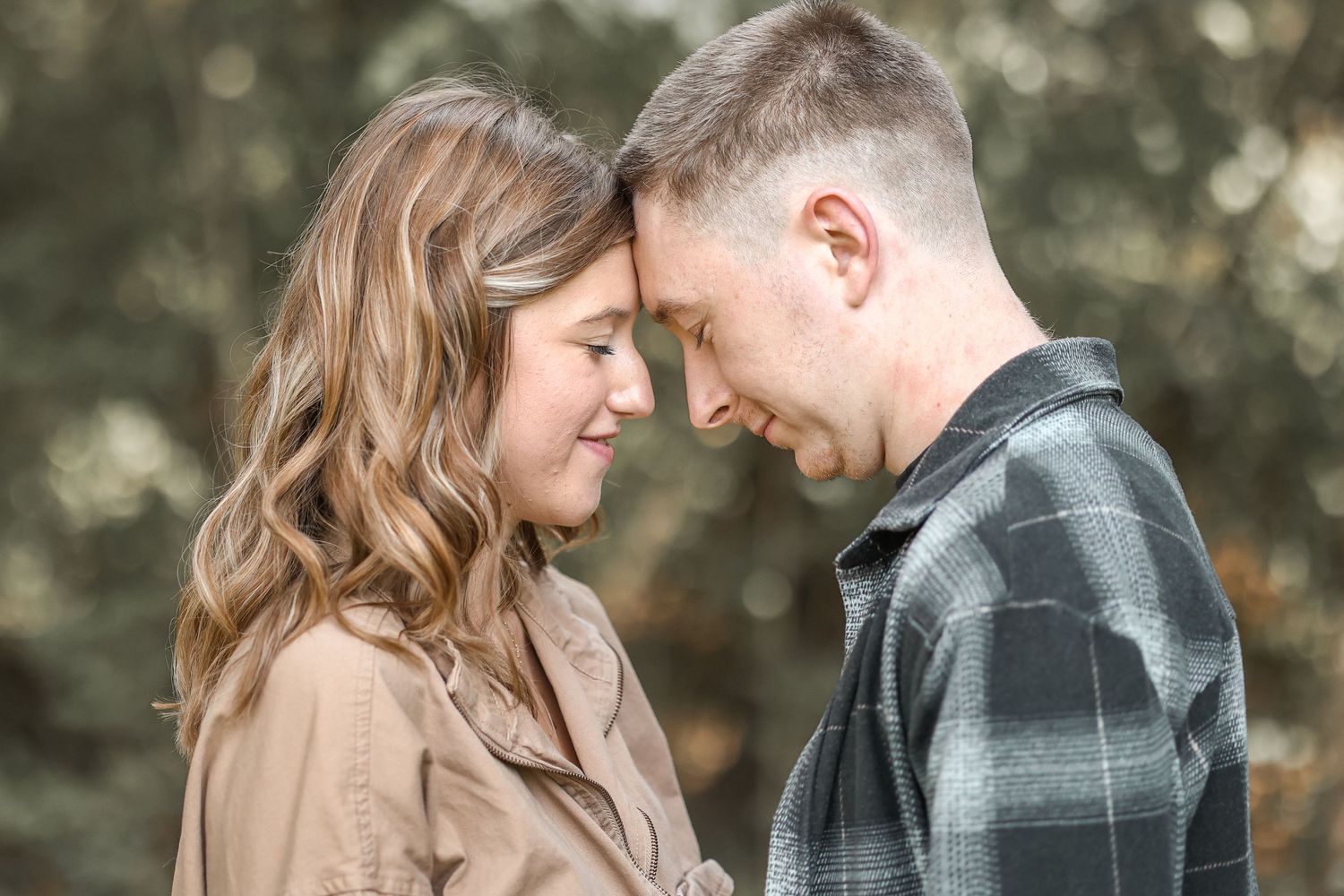 Intimate moment between couple touching foreheads against blurred natural background.