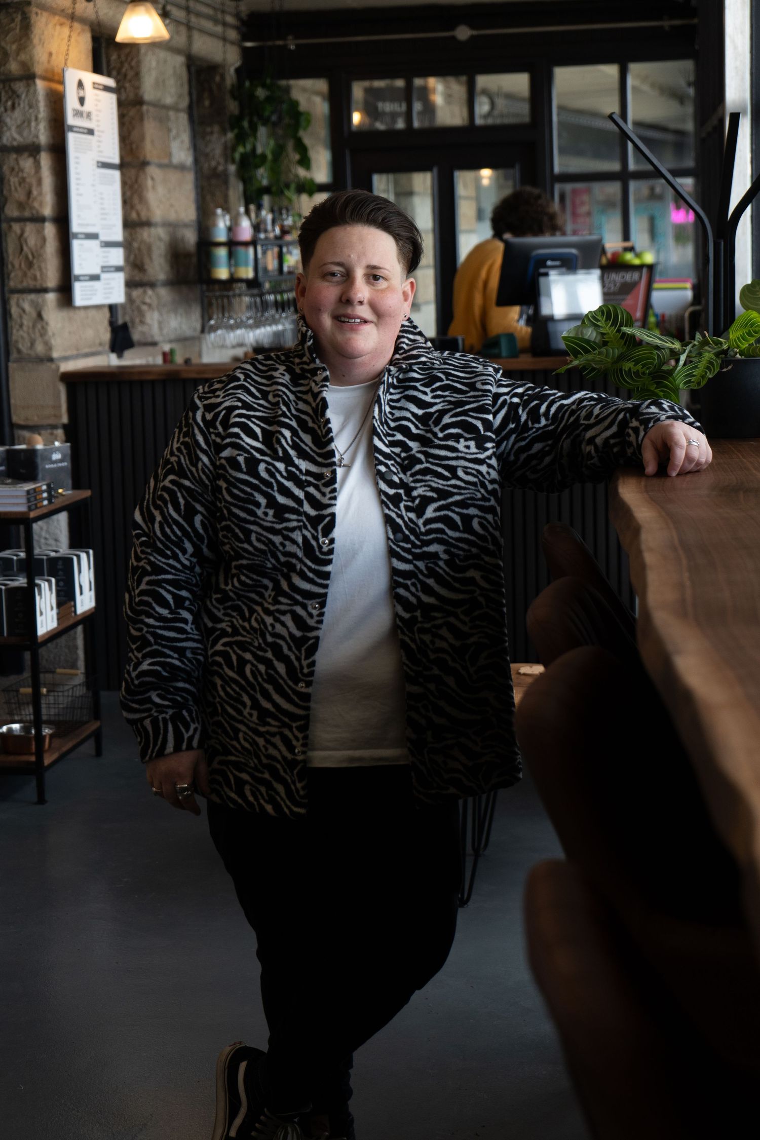 Person in patterned jacket seated at rustic wooden table in industrial-style space.