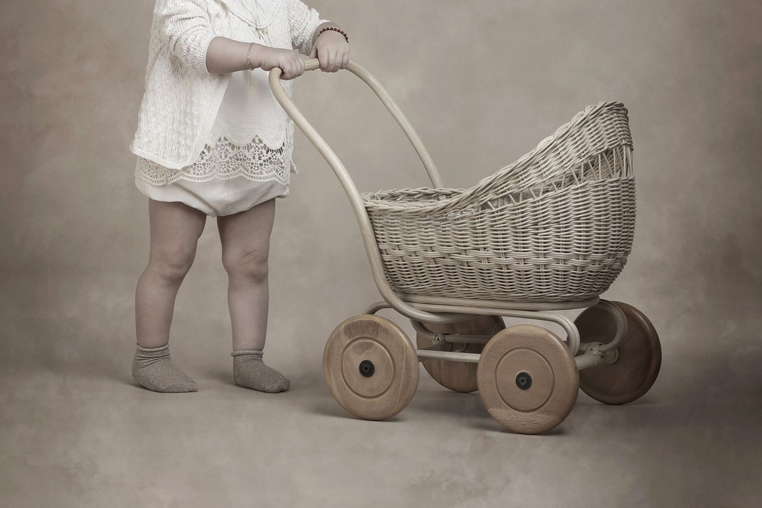 An antique woven wicker baby carriage with wooden wheels on a sepia background.