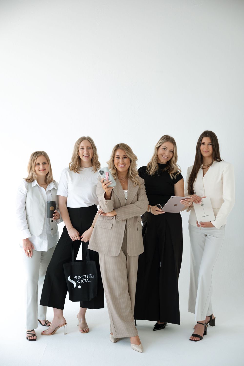 A group of women pose together wearing coordinated black and white business attire in a minimalist studio setting.