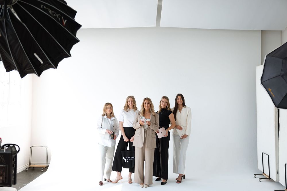 Behind the scenes fashion photoshoot setup showing lighting equipment and models against a white studio backdrop.