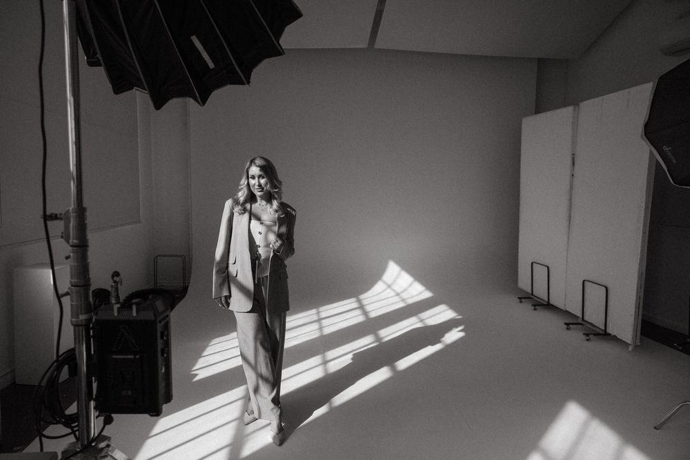 A model stands in dramatic lighting during a professional fashion photoshoot in a studio space.