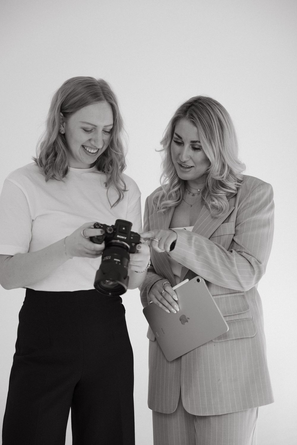 Two people in professional attire reviewing photos on a digital camera in a black and white photograph.