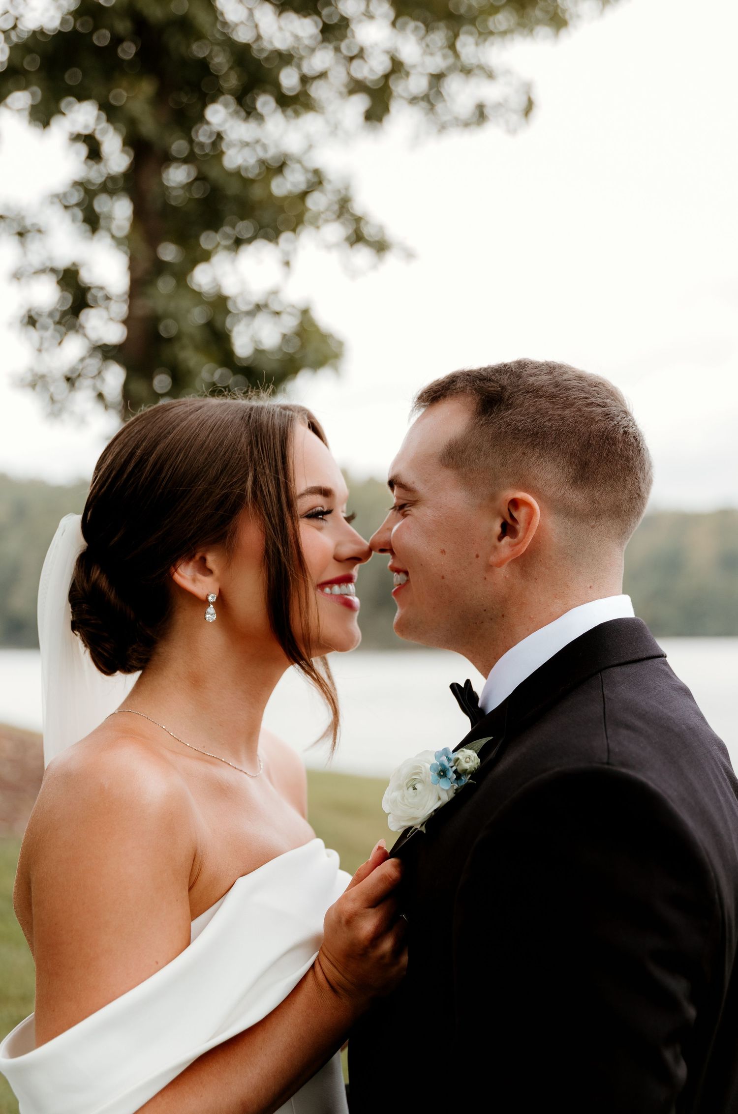 lose-up of newlyweds Mallory and Brady sharing a tender moment by a serene lake, surrounded by soft focus trees.
