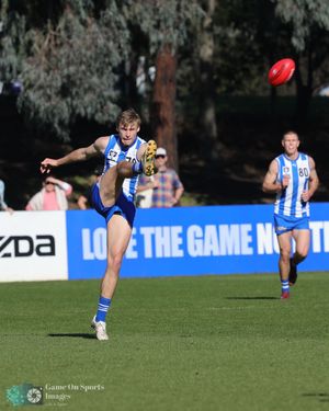 AFL player kicks the red football during a match with Mazda advertising boards visible in the background.