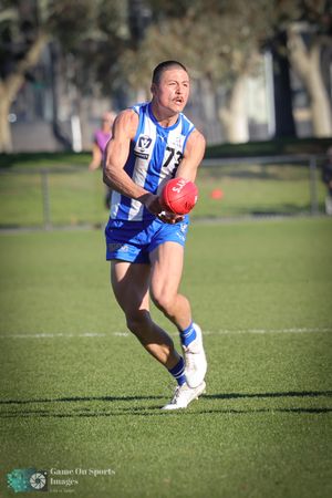 Australian rules football player in blue and white striped jersey runs with red ball during sunny match on grass field.
