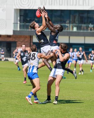 Several Australian rules football players leap high to contest for a mark during a competitive match on a grass field.