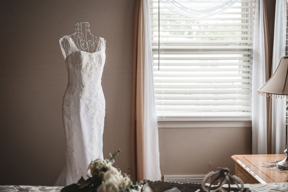 White lace wedding dress hanging by window with natural light streaming in.