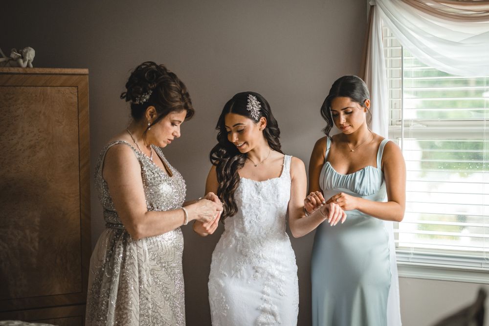 Wedding party helping with dress preparations in a sunlit room.