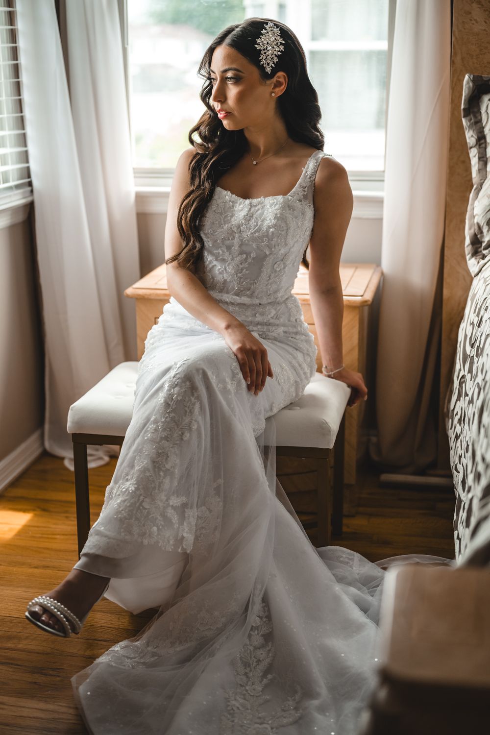 Bride in detailed lace gown posing gracefully by window in warm sunlight.